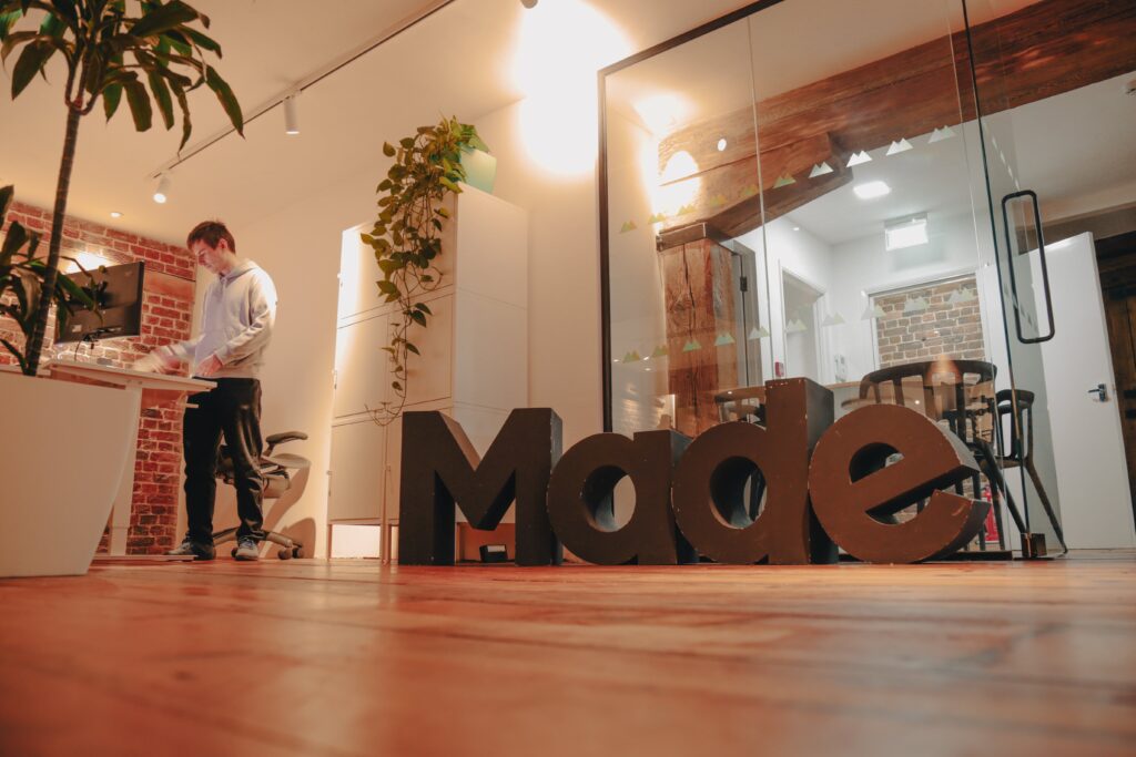 Person standing and working at a desk next to a large sign that reads Made